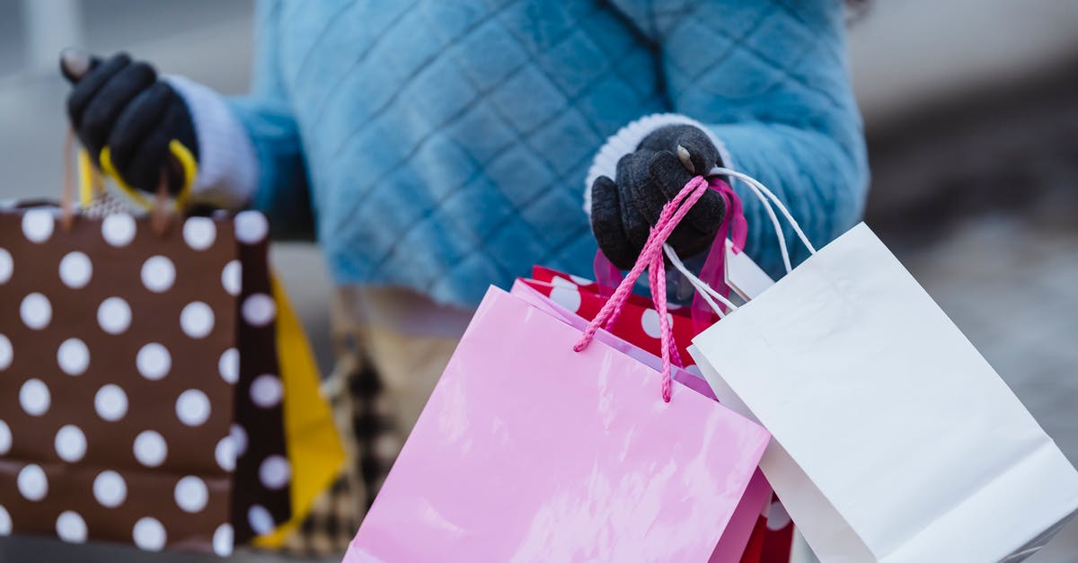 1-week holiday in Fiji. How to carry my cash? - Crop anonymous female in blue soft sweater with many different colorful gift bags on blurred background 1-week holiday in Fiji. How to carry my cash? - Crop anonymous female in blue soft sweater with many different colorful gift bags on blurred background