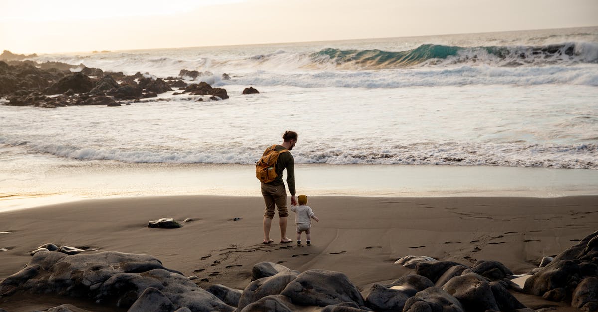 3-4 months infant travel: 1 long trip (13 hours) or 3 medium trips (6+6+4 hours) [closed] - Unrecognizable young father with little child walking on beach