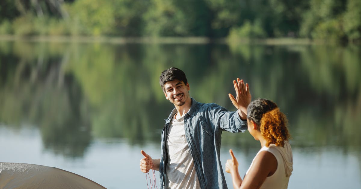 3-month trip to California - Do I give my bank my Social Security Number? [closed] - Happy young traveling couple giving each other high five while standing on river bank and putting up tent