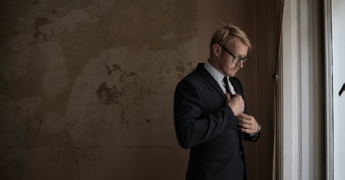 A refund that I think my agent wants to cheat me on - Side view of male realtor in formal wear bowing head and straightening tie while standing near windowsill in old building A refund that I think my agent wants to cheat me on - Side view of male realtor in formal wear bowing head and straightening tie while standing near windowsill in old building