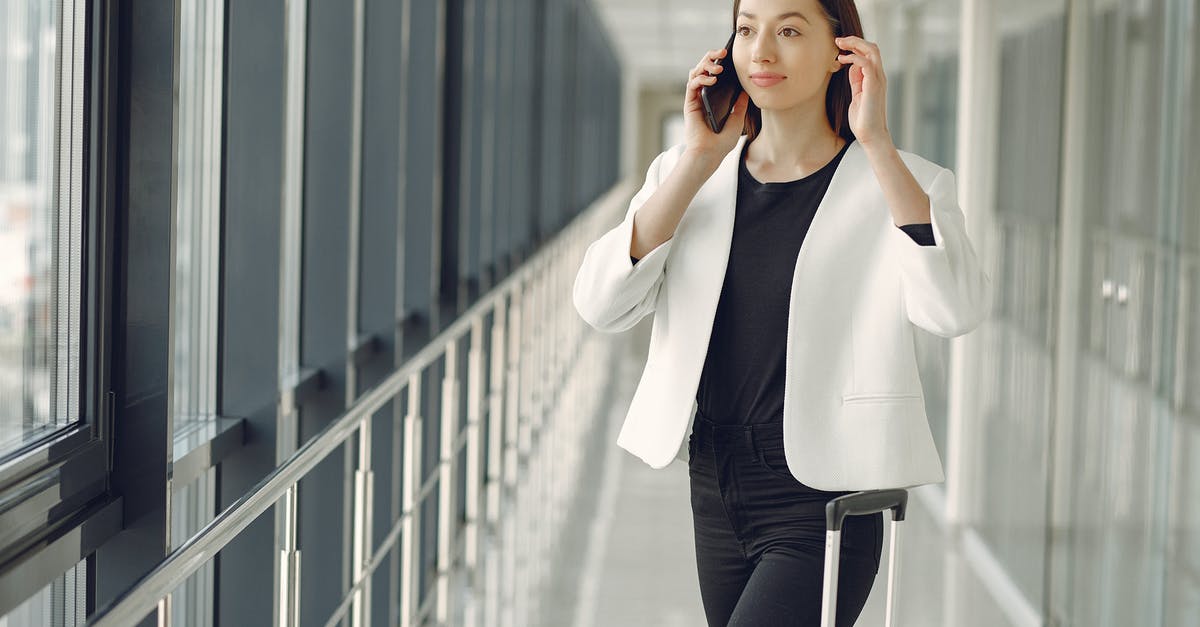 About the baggage formalities at Delhi airport during a travel between Tokyo and Ahmedabad and vice versa [closed] - Positive young businesswoman in stylish formal wear with suitcase talking on smartphone and standing in modern airport corridor while waiting for flight