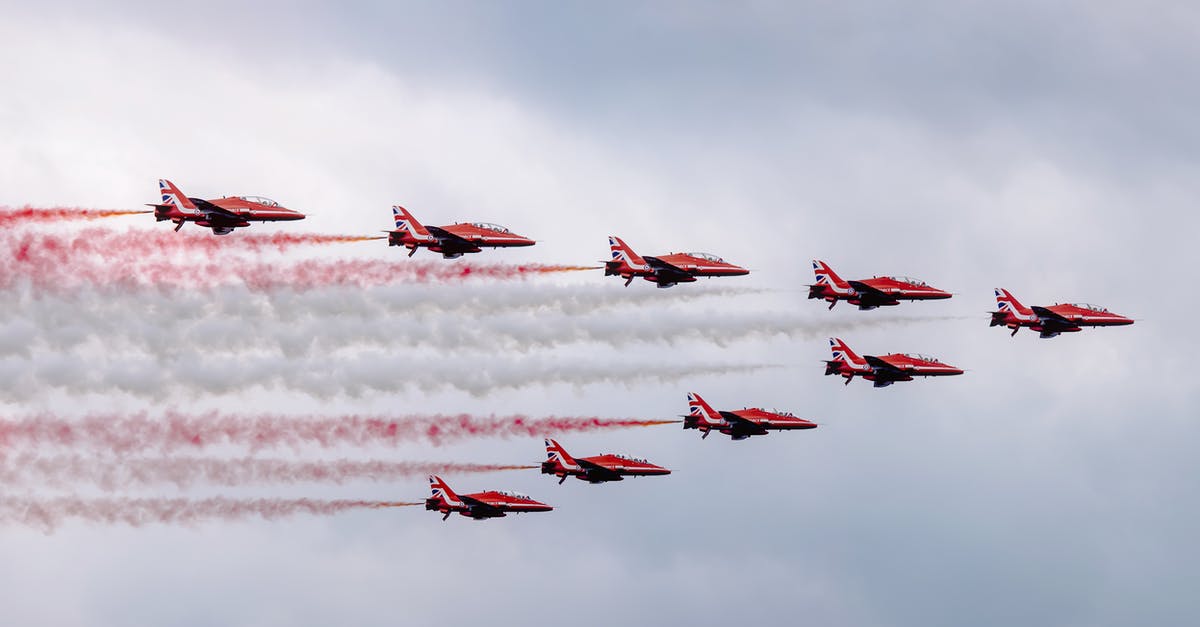 Airlines actions for overbooking a flight - Low angle of modern red military aircraft flying in cloudy sky symmetrically and creating lines with color smokes during air show Airlines actions for overbooking a flight - Low angle of modern red military aircraft flying in cloudy sky symmetrically and creating lines with color smokes during air show