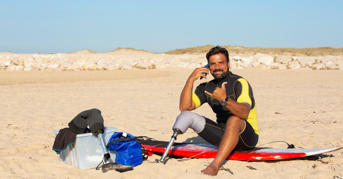 Airlines with the most Surfboard friendly baggage policy & fees pricing? - Male with prosthesis looking at camera sitting on surfboard while having conversation on smartphone and showing shaka Airlines with the most Surfboard friendly baggage policy & fees pricing? - Male with prosthesis looking at camera sitting on surfboard while having conversation on smartphone and showing shaka