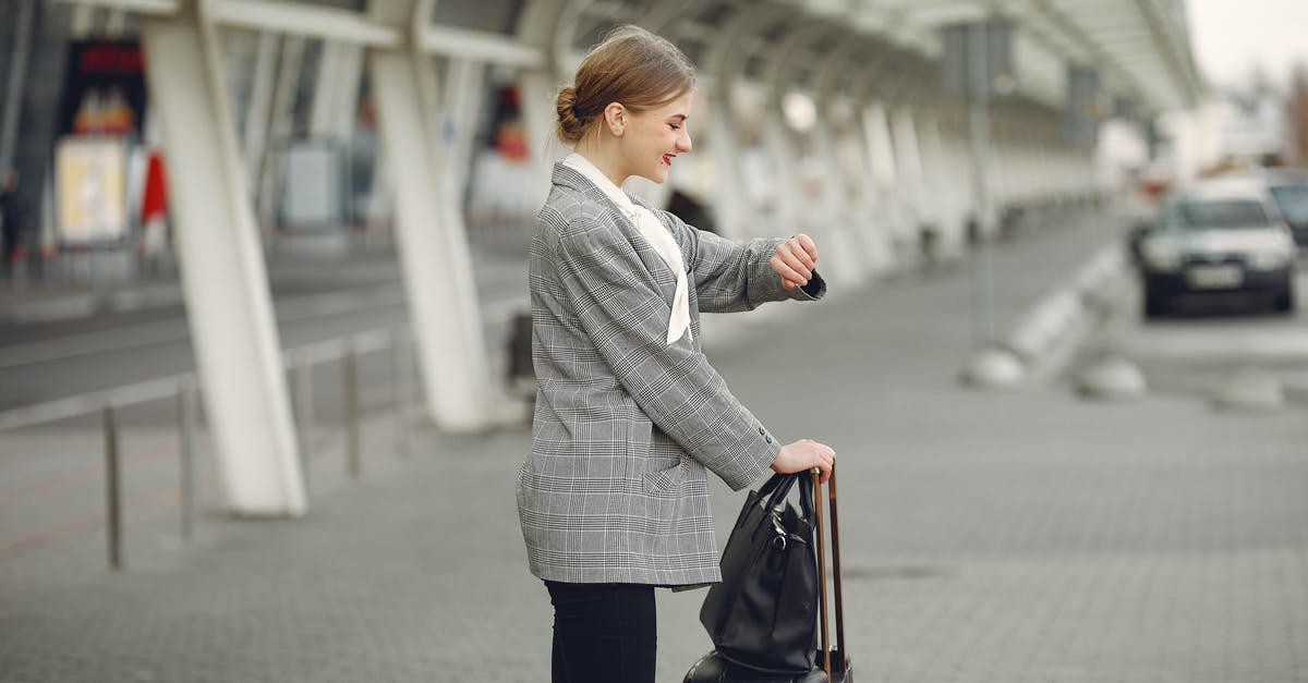Airport transfer in Manila between Terminals 1 and 3 - Cheerful female manager checking time on wristwatch standing with bags near bus station Airport transfer in Manila between Terminals 1 and 3 - Cheerful female manager checking time on wristwatch standing with bags near bus station