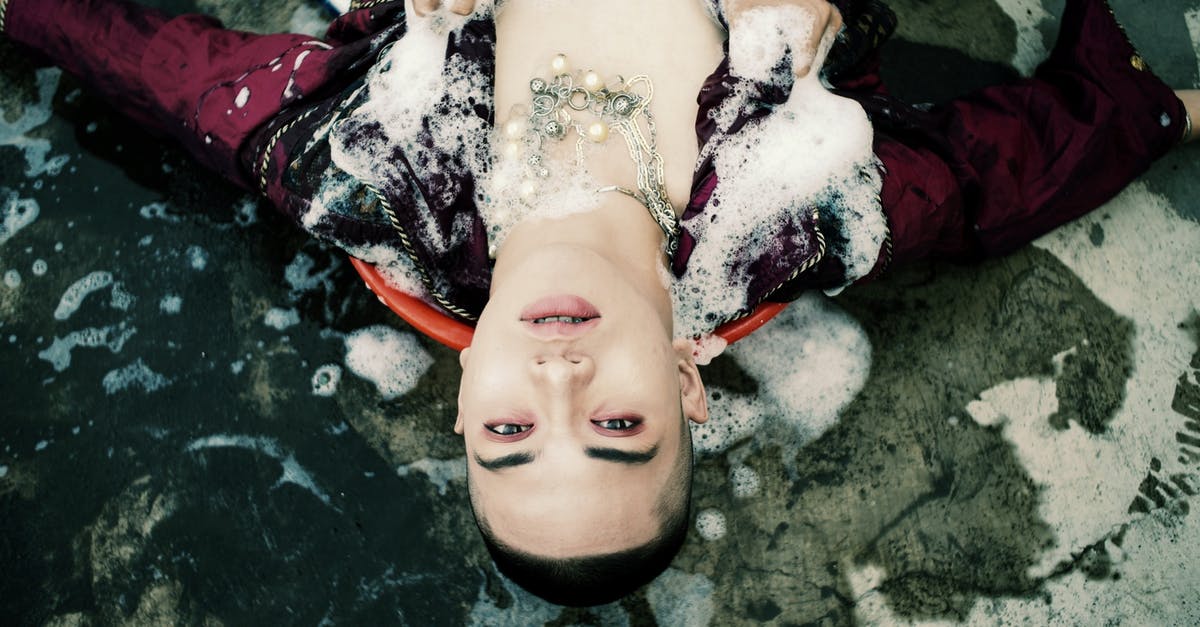 Am I likely to get problems travelling abroad from the UK when my gender appearance doesn't match my passport - Top view of unrecognizable person touching young male model covered with white foam and lying on concrete ground