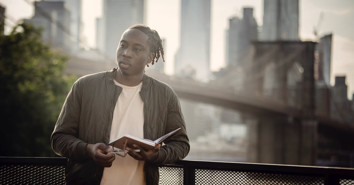 American with expired student visa traveling in Schengen zone - Young pensive African American male in casual clothes with open diary in hands leaning on balcony railing and looking away against blurred Brooklyn Bridge in summertime American with expired student visa traveling in Schengen zone - Young pensive African American male in casual clothes with open diary in hands leaning on balcony railing and looking away against blurred Brooklyn Bridge in summertime