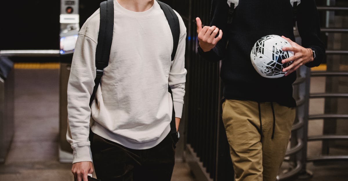 An active underground city/village? - Crop young male friends wearing casual clothes with backpacks and soccer ball walking in modern underground station and chatting An active underground city/village? - Crop young male friends wearing casual clothes with backpacks and soccer ball walking in modern underground station and chatting