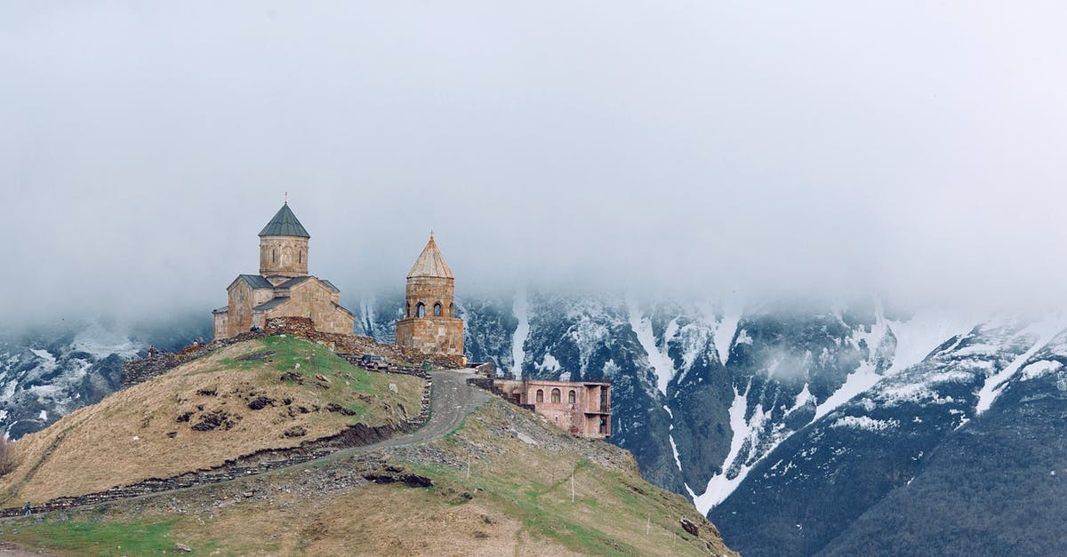 Applying for a Georgia tourism visa - Medieval church on grassy hilltop surrounded by majestic mountains Applying for a Georgia tourism visa - Medieval church on grassy hilltop surrounded by majestic mountains