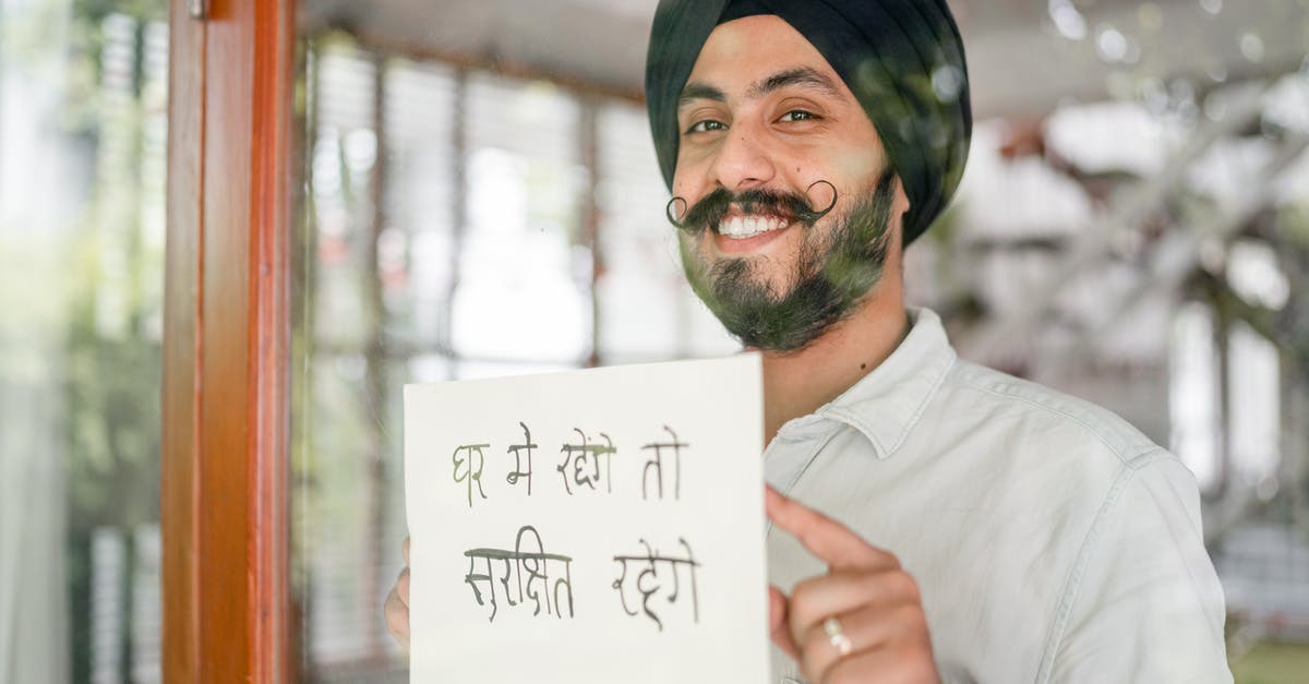 Are airlines required to give the safety briefing in another language if asked? - Positive mature modern Sikh male in turban with curly mustache leaning against glass wall with sign in indian on paper sheet and looking at camera