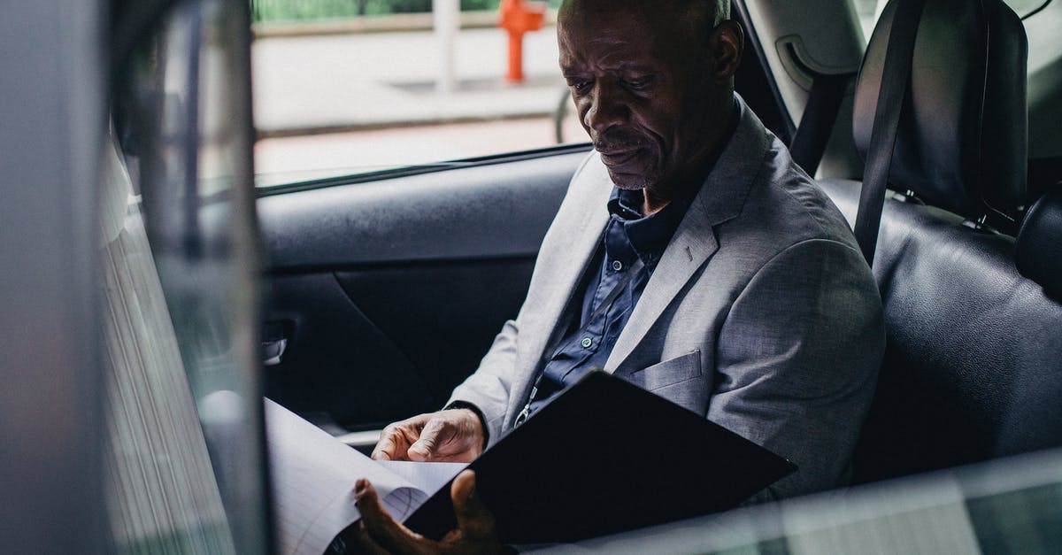 Are car rental contracts provided in English? - Side view serious African American businessman in formal clothes sitting in car back seat and reading documents Are car rental contracts provided in English? - Side view serious African American businessman in formal clothes sitting in car back seat and reading documents