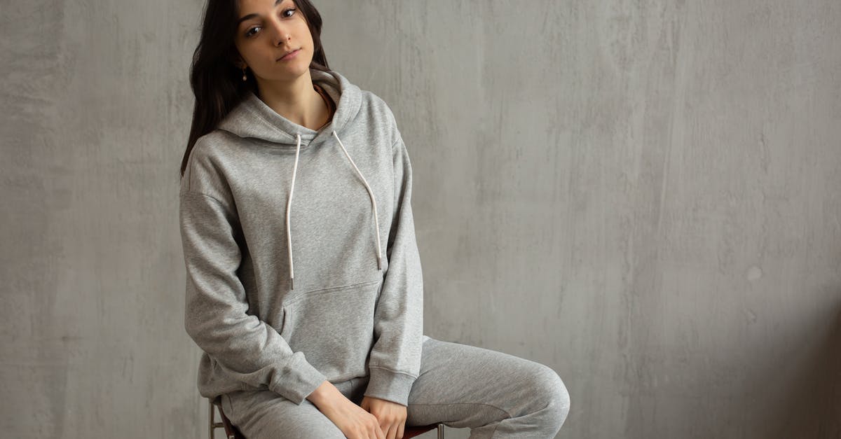 Are sweatpants frowned upon on flights? - Young female in gray sports suit sitting on chair against concrete wall and looking at camera Are sweatpants frowned upon on flights? - Young female in gray sports suit sitting on chair against concrete wall and looking at camera