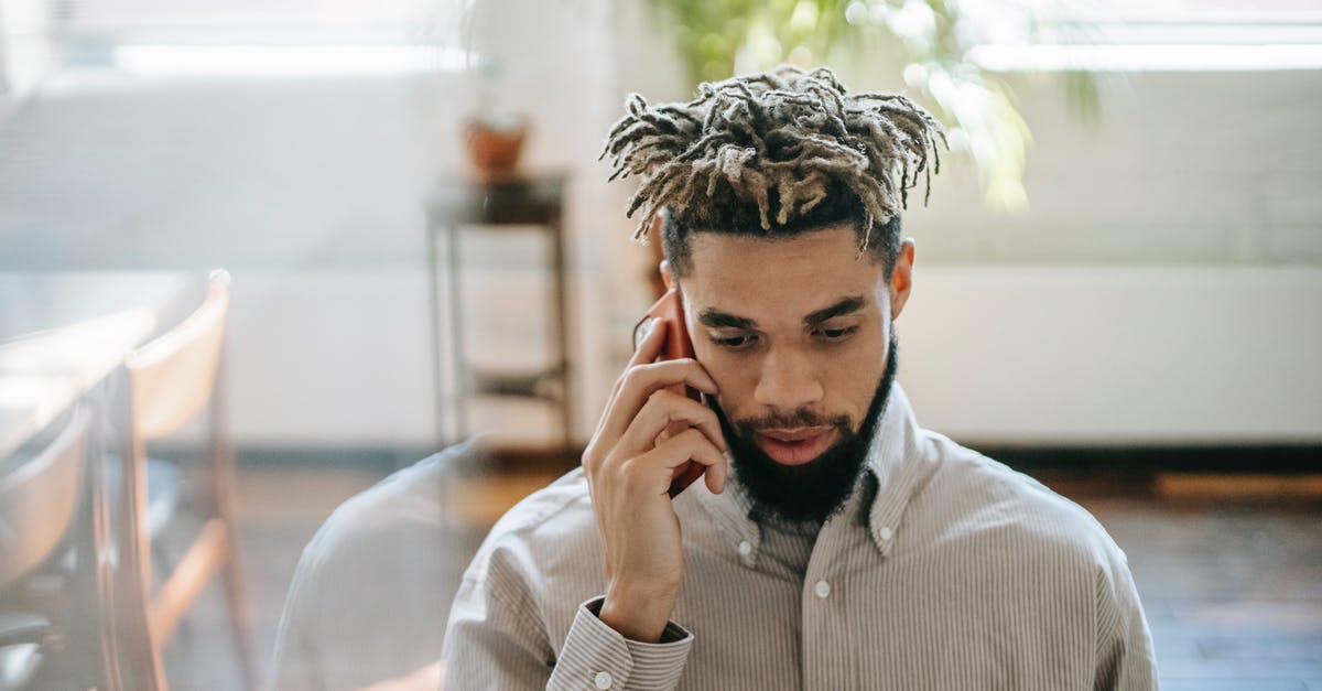 Are there any RED flags raised when we call UK Home Office for settlement visa status update? [closed] - Black man in casual outfit speaking on cellphone in light room near table with window and plant on background