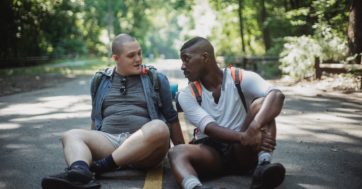Are there certain countries that a black African traveler should avoid travelling to? [closed] - Calm diverse homosexual couple with travel backpacks sitting on asphalt roadway and looking at each other in sunny day