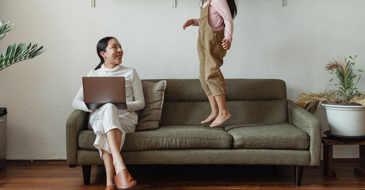 Are there some places I can stay for free in South Korea besides couch surfing? - Smiling Asian mother in casual wear working on laptop while cute daughter jumping on couch in cozy living room