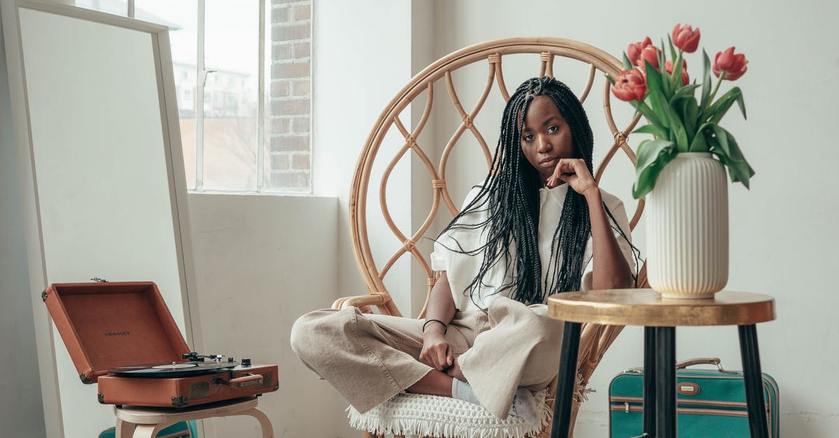 At Schengen entry points, is a record kept of visa-free entry? - Serious young African American female millennial sitting on bamboo chair with crossed legs near table with vase of fresh tulips and listening to music via vinyl record