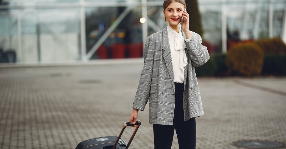 Atlanta Terminal Change: Domestic to International with Bags - Stylish businesswoman speaking on smartphone while standing with luggage near airport