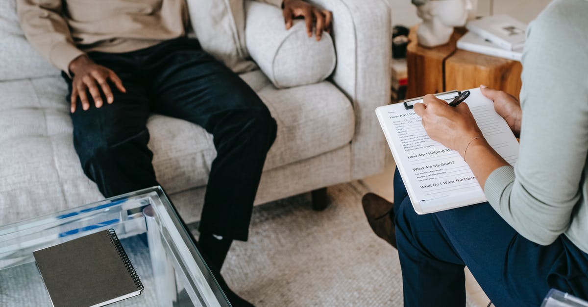 Available help for voluntary departure from the UK - From above crop African American male in casual clothes sitting on comfy couch and answering professional female consultant questions in modern psychotherapy office Available help for voluntary departure from the UK - From above crop African American male in casual clothes sitting on comfy couch and answering professional female consultant questions in modern psychotherapy office