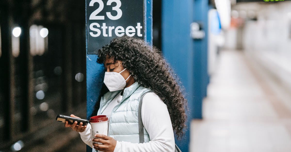 Barbados via JFK - Transit on Media Visa - Focused African American female wearing casual outfit and protective mask standing on New York underground platform with takeaway coffee and using mobile phone Barbados via JFK - Transit on Media Visa - Focused African American female wearing casual outfit and protective mask standing on New York underground platform with takeaway coffee and using mobile phone