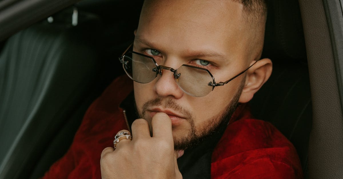 Best seat for sleeping on megabus red-eye trip in USA? [closed] - Pensive young unshaven male in eyeglasses and red jacket sitting on driver front seat of car and looking at camera