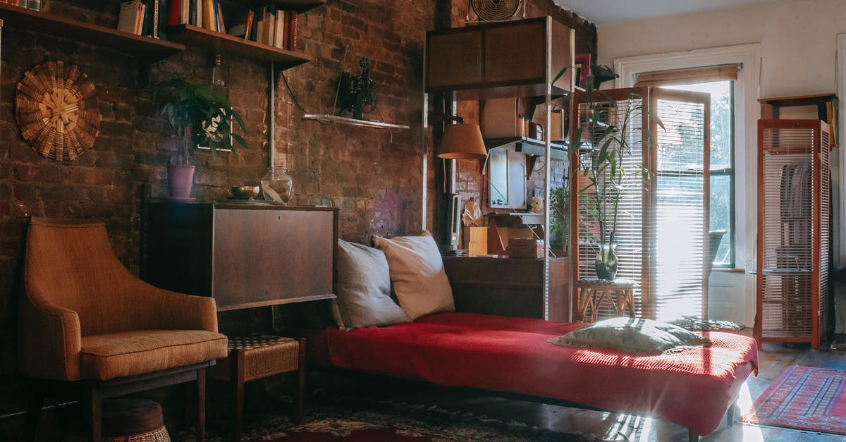 Booking accommodation for long term (few months) - Vintage styled bedroom interior with classic wooden furniture and bookshelves decorated weathered brick wall near comfortable bed and armchair Booking accommodation for long term (few months) - Vintage styled bedroom interior with classic wooden furniture and bookshelves decorated weathered brick wall near comfortable bed and armchair