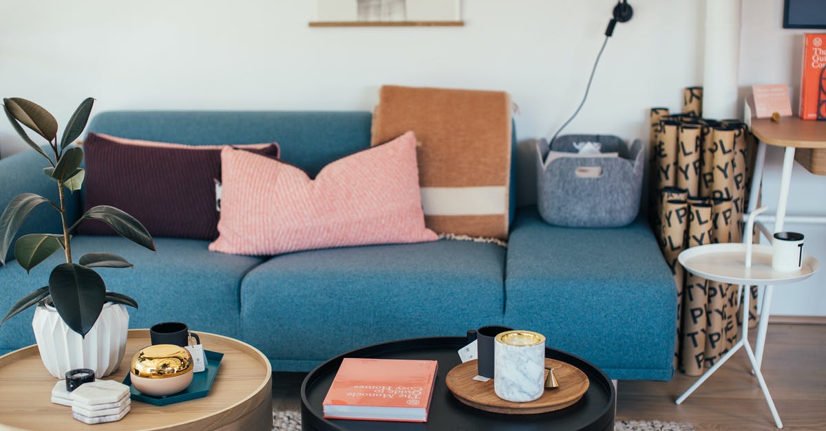 Booking last minute accommodation in Ireland - Comfortable sofa with cushions placed in cozy living room near small round coffee tables decorated with potted plant and candles Booking last minute accommodation in Ireland - Comfortable sofa with cushions placed in cozy living room near small round coffee tables decorated with potted plant and candles