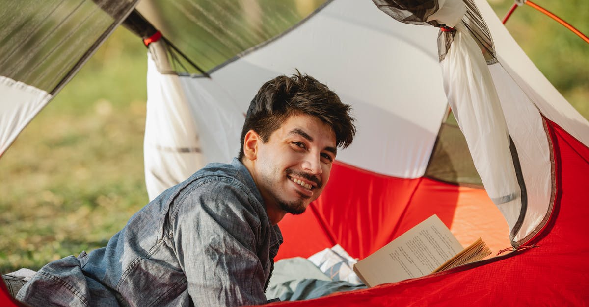 Booking repeat round trip every weekend - Side view of cheerful adult male hiker lying with textbook in tent and looking forward in sunlight Booking repeat round trip every weekend - Side view of cheerful adult male hiker lying with textbook in tent and looking forward in sunlight