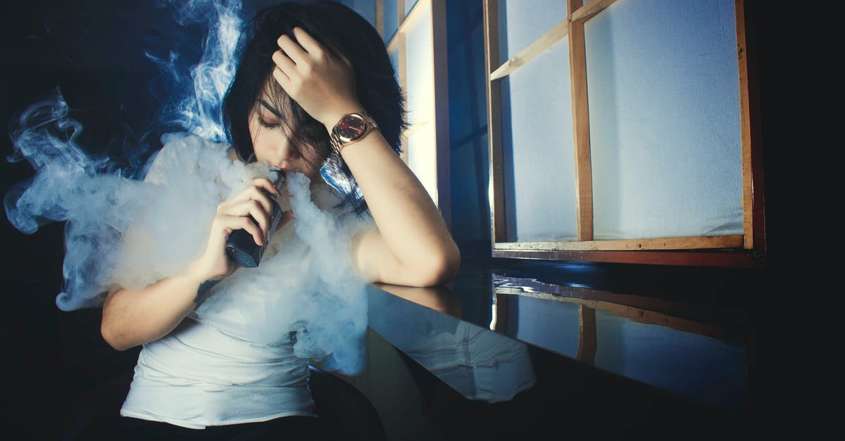 Bringing nicotine e-liquids to Australia - Cool casual brunette in white t shirt smoking electronic cigarette while leaning on hand in dark studio Bringing nicotine e-liquids to Australia - Cool casual brunette in white t shirt smoking electronic cigarette while leaning on hand in dark studio
