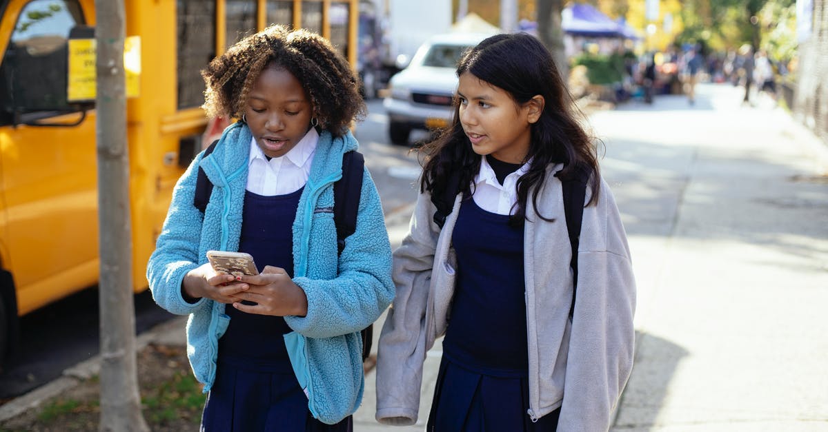 Bus times from Anuradhapura to Kandy? - Cheerful multiracial girls classmates with backpacks browsing smartphone while walking together on sunny autumn street near yellow school bus Bus times from Anuradhapura to Kandy? - Cheerful multiracial girls classmates with backpacks browsing smartphone while walking together on sunny autumn street near yellow school bus