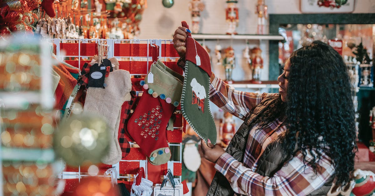 Buying Holi accessories after the event has ended - Side view of smiling African American female with Xmas sock in shop with decorative baubles and gifts Buying Holi accessories after the event has ended - Side view of smiling African American female with Xmas sock in shop with decorative baubles and gifts