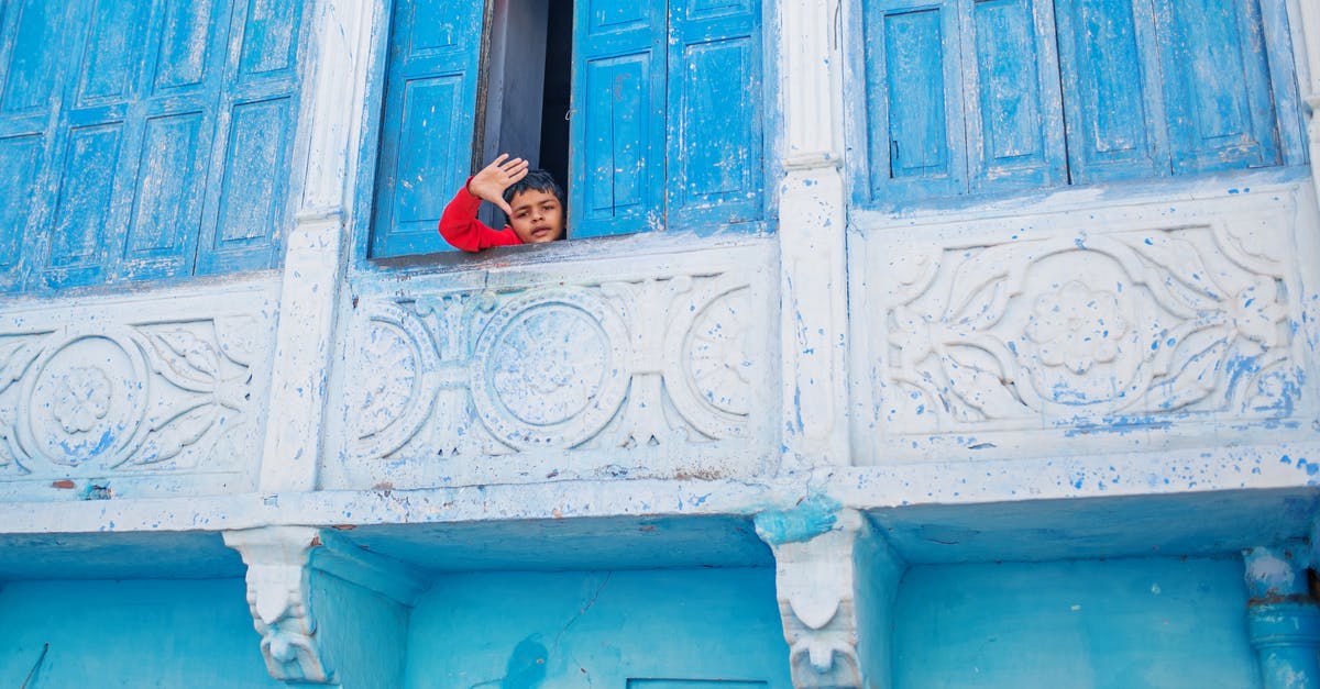 Can a child enter the UK on an accompanied visa and then leave the country alone? - From below of little ethnic boy waving at camera standing behind shabby shutters of blue balcony Can a child enter the UK on an accompanied visa and then leave the country alone? - From below of little ethnic boy waving at camera standing behind shabby shutters of blue balcony