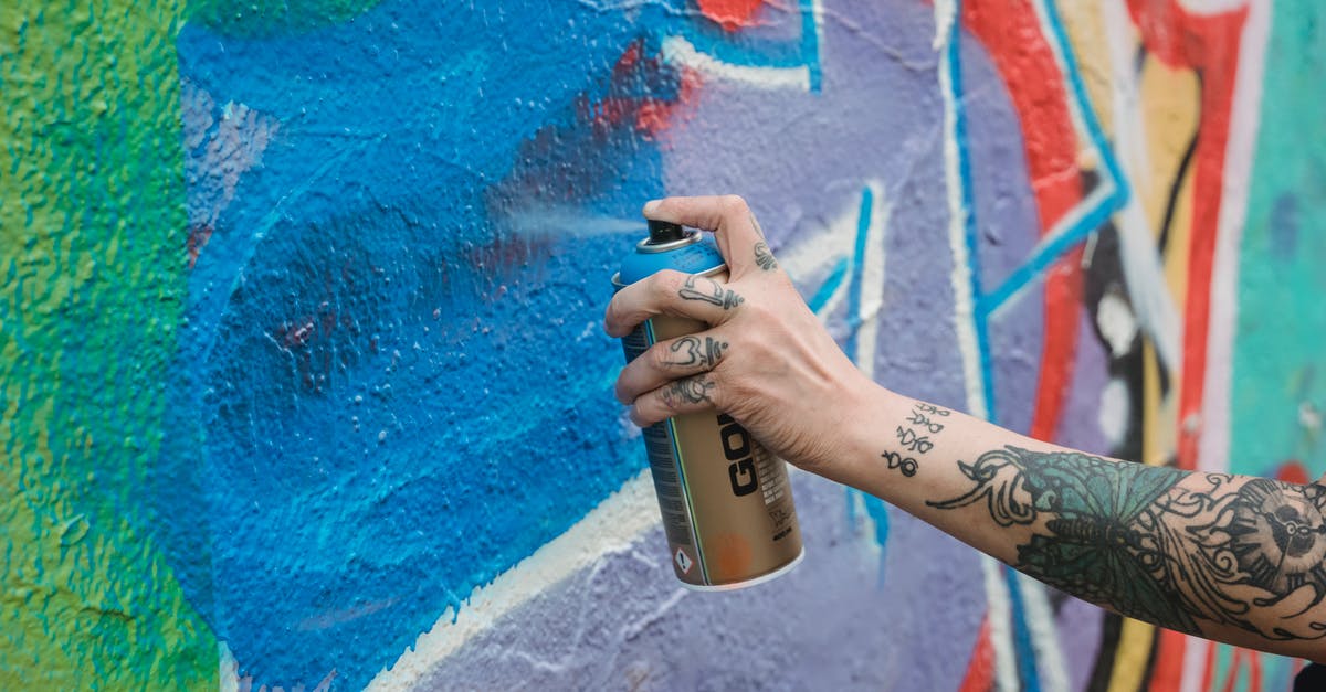 Can a husband/wife apply for UK Visas with different validities? - Crop unrecognizable tattooed painter spraying blue paint from can on multicolored wall with creative graffiti while standing on street in city