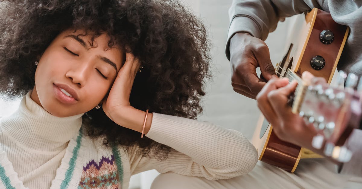 Can a musician missing their instrument at home visit music shops purely to play in-store, not to buy? [closed] - Satisfied African American female with closed eyes listening to anonymous black boyfriend playing song on acoustic guitar while spending time together