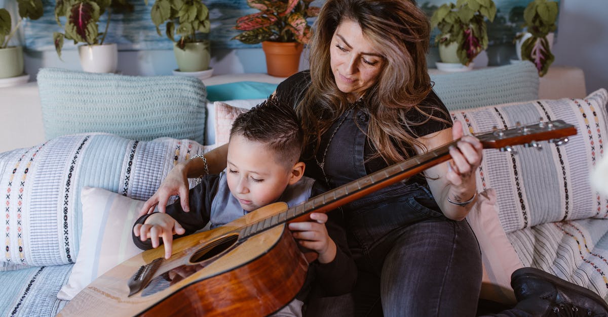 Can a musician missing their instrument at home visit music shops purely to play in-store, not to buy? [closed] - Relaxed young woman playing guitar on bed with little son