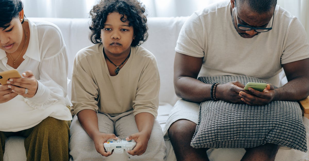 Can American mother living in France bring French father with her to the US right now? [duplicate] - Focused ethnic child playing video game with joystick sitting on sofa between divers parents browsing smartphones