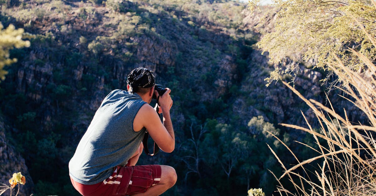 Can anyone recognise the location and uniforms in these pictures - Back view of busy male photographer in summer clothes squatting on edge of hill and taking picture of nature while travelling at daytime Can anyone recognise the location and uniforms in these pictures - Back view of busy male photographer in summer clothes squatting on edge of hill and taking picture of nature while travelling at daytime