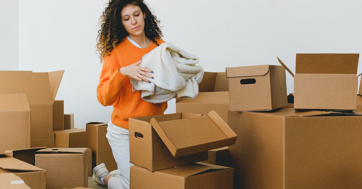 Can I bring a new laptop in its package into the plane as carry-on? - Focused young relocating female packing belonging into cardboard boxes