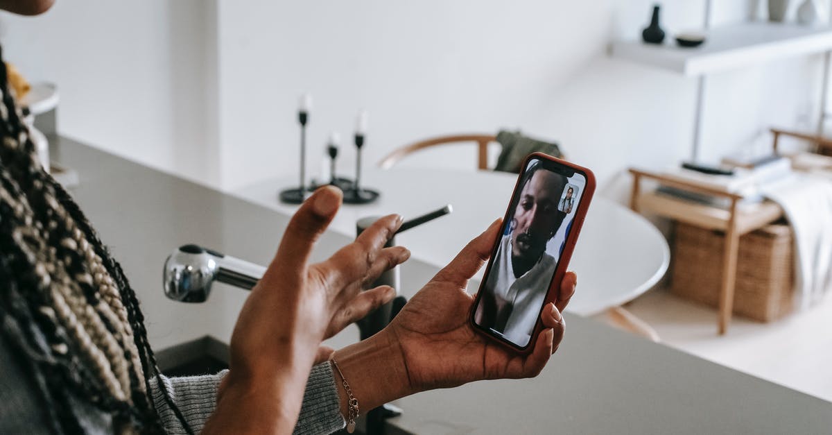 Can I call the airport to see if my boyfriend made it through customs? - High angle of crop unrecognizable young black female gesticulating while having video conversation on smartphone with boyfriend in kitchen
