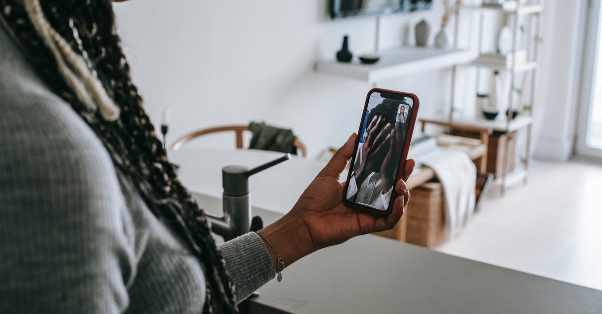 Can I call the airport to see if my boyfriend made it through customs? - Crop unrecognizable African American lady with long braids having video call on mobile phone with upset boyfriend covering face with hands while standing in modern kitchen