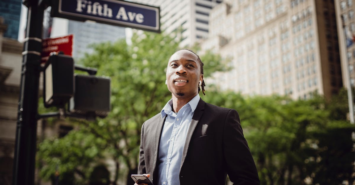 Can I carry 5 mobile phones to US from India? - From below of young handsome black male in smart suit listening to music and waiting for car to pass while standing near street sign in Manhattan on sunny day Can I carry 5 mobile phones to US from India? - From below of young handsome black male in smart suit listening to music and waiting for car to pass while standing near street sign in Manhattan on sunny day
