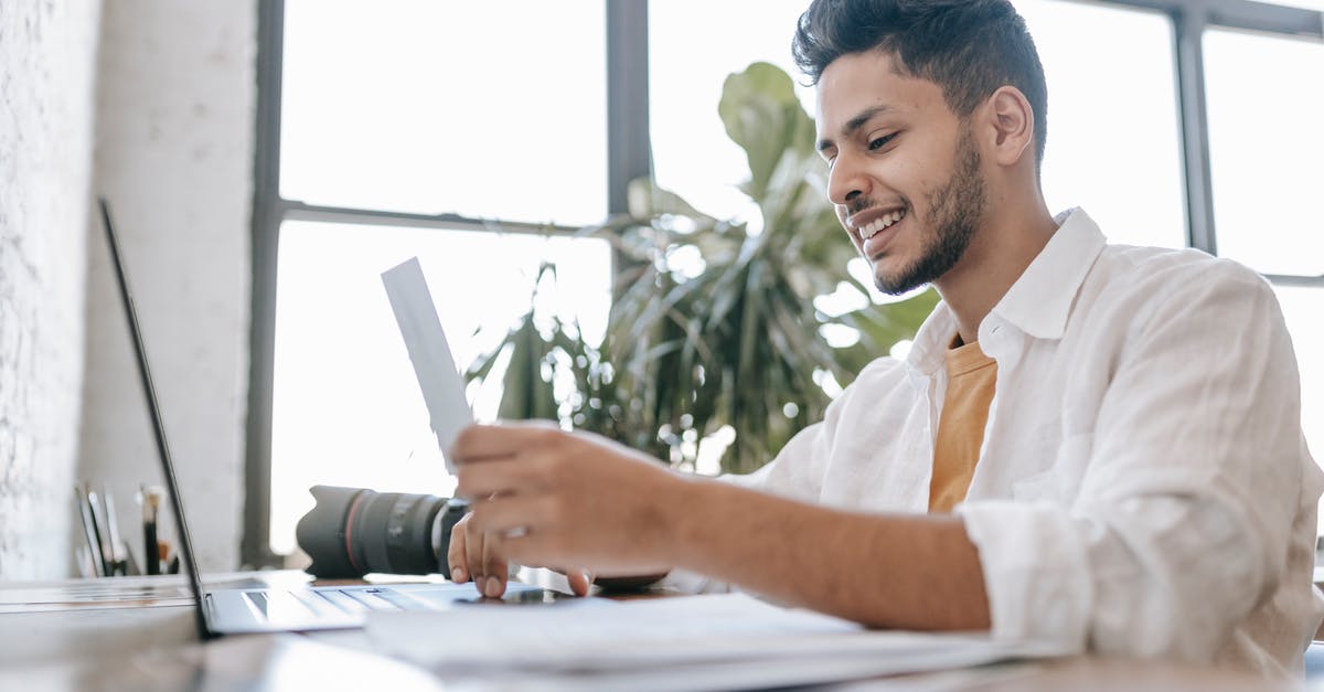 Can I cross the border into Canada using my birth certificate and a photo ID? - Happy ethnic man looking at printed picture at desk Can I cross the border into Canada using my birth certificate and a photo ID? - Happy ethnic man looking at printed picture at desk