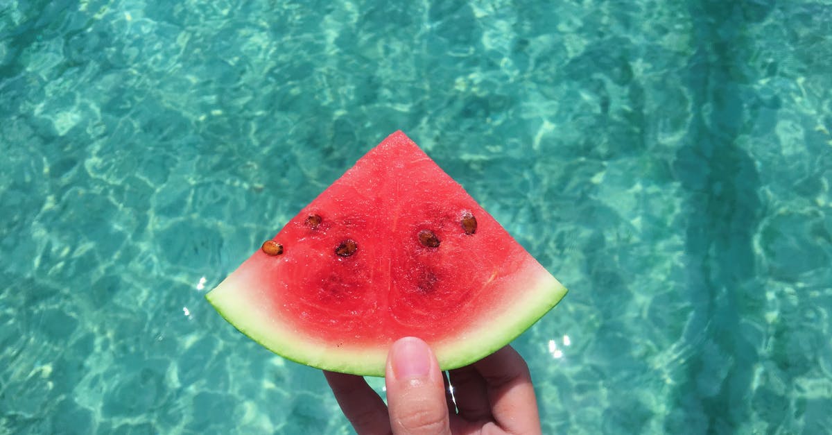 Can I have a watermelon in hand luggage? - Hand Holding a Slice of Watermelon With Blue Swimming Pool Water in the Background Can I have a watermelon in hand luggage? - Hand Holding a Slice of Watermelon With Blue Swimming Pool Water in the Background