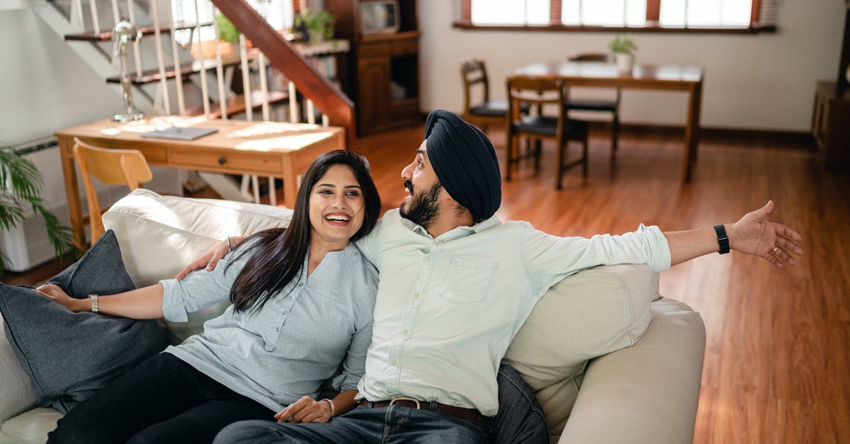 Can I live in Berlin comfortably for one month with 1,000 euros if housing is free? [closed] - Happy adult ethnic man embracing wife and showing new housing while ethnic couple in casual clothes sitting on comfortable couch in living room