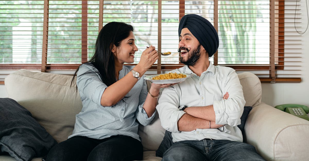 Can I live in Berlin comfortably for one month with 1,000 euros if housing is free? [closed] - Positive Indian female in casual wear sitting on sofa in living room and feeding bearded male in turban