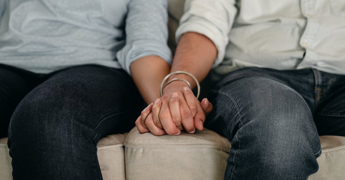 Can I live in Berlin comfortably for one month with 1,000 euros if housing is free? [closed] - Crop anonymous man in jeans and shirt with wristband holding females hand while resting together on cozy couch in apartment