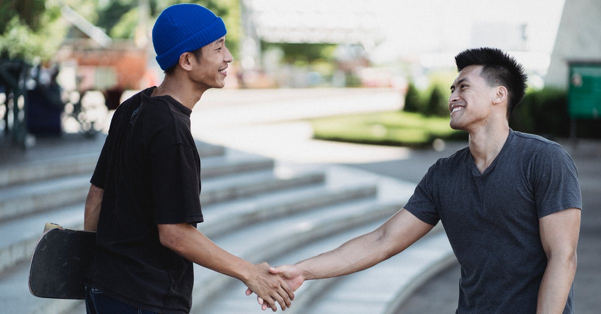 Can I meet my friend during a connecting flight? (LHR) - Cheerful young Asian men in street wear shaking hands and greeting each other with friendly smile Can I meet my friend during a connecting flight? (LHR) - Cheerful young Asian men in street wear shaking hands and greeting each other with friendly smile