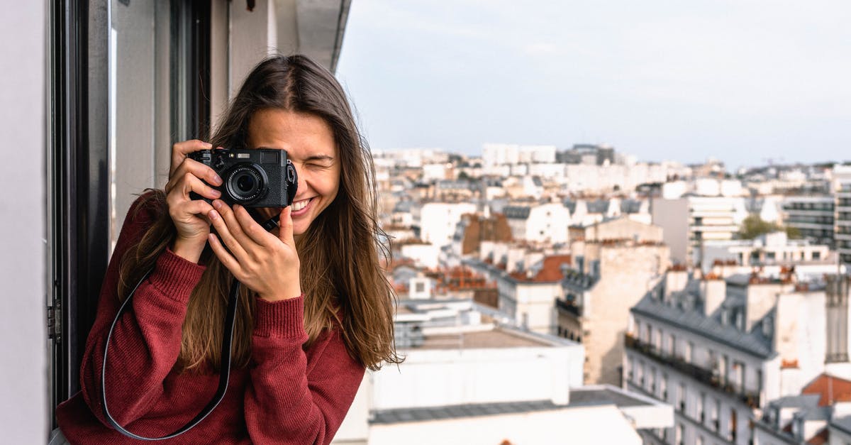 Can I sell the photographs I take on a tourist visa? - Woman Wearing Maroon Sweater Standing on Veranda Using Camera While Smiling Overlooking Houses and Buildings Can I sell the photographs I take on a tourist visa? - Woman Wearing Maroon Sweater Standing on Veranda Using Camera While Smiling Overlooking Houses and Buildings