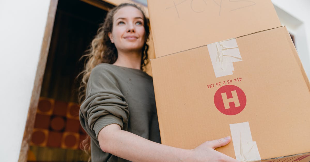 Can I ship my stuff from London to New York storage facility and pick it up later? [closed] - Confident young lady in casual wear carrying heavy carton boxes with toys and looking away while leaving old house