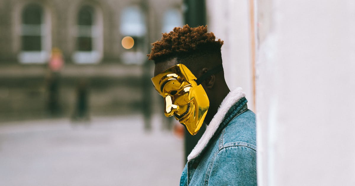 Can I side-step discrimination against foreigners in Japan? - Side view of thoughtful African American activist wearing golden Anonymous mask as symbol of protest against current state policy standing near building on city street in daytime Can I side-step discrimination against foreigners in Japan? - Side view of thoughtful African American activist wearing golden Anonymous mask as symbol of protest against current state policy standing near building on city street in daytime