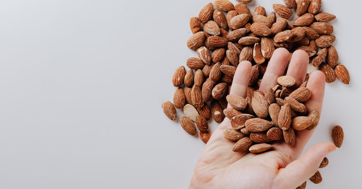 Can I take camping food in hand luggage? - From above of anonymous male taking tasty organic almonds from pile of nuts placed on white background isolated illustrating healthy food concept Can I take camping food in hand luggage? - From above of anonymous male taking tasty organic almonds from pile of nuts placed on white background isolated illustrating healthy food concept