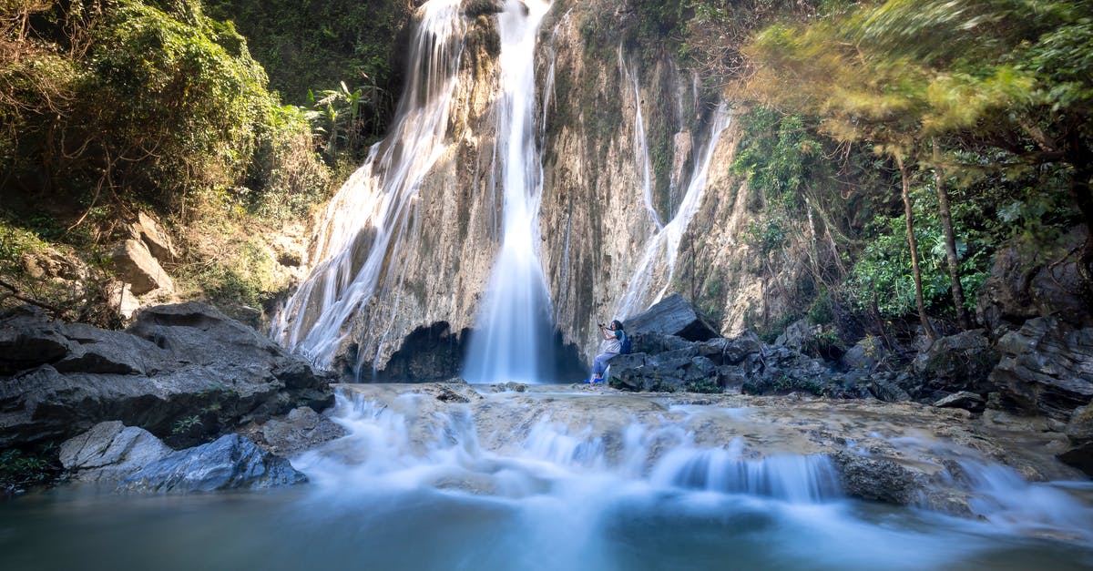 Can I travel to Australia on a business trip using my tourist stream visitor visa? [duplicate] - Side view of anonymous backpacker taking photo of foamy waterfall on camera while standing between ridge and pond